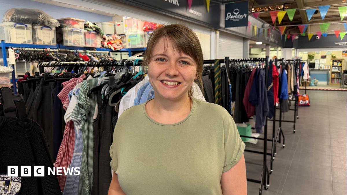 Ashleigh Hirst standing in the charity's uniform store, smiling at the camera. She has brown hair tied back and a fringe. She is wearing a green T-shirt.