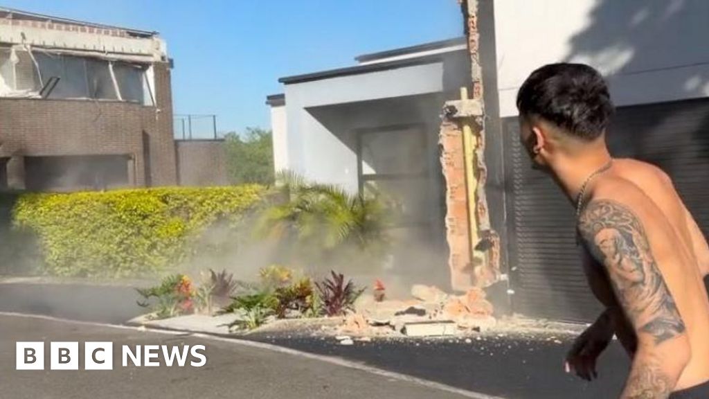 A topless man stands in the street while an earthquake damages buildings around him