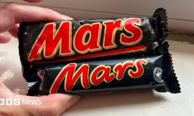 A Mars Bar from 1991 and a modern-day one held next to each other. The old Mars Bar is considerably bigger.