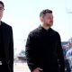 Andy Burnham and Volodymyr Zelensky walk next to each other at a naval base. Both men are dressed in black and have short, dark hair. Burnham is wearing glasses. Military personnel can be seen in the background.
