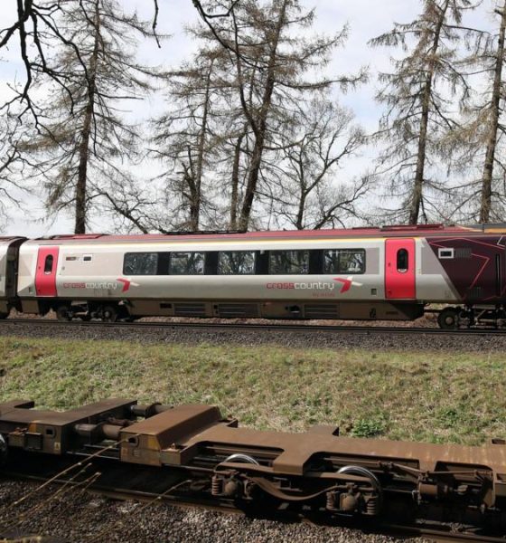 The cab and first carriage of a CrossCountry train travels on tracks in the countryside. In the background trees and fields can be seen.