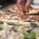 A robot arm hovers over a pizza