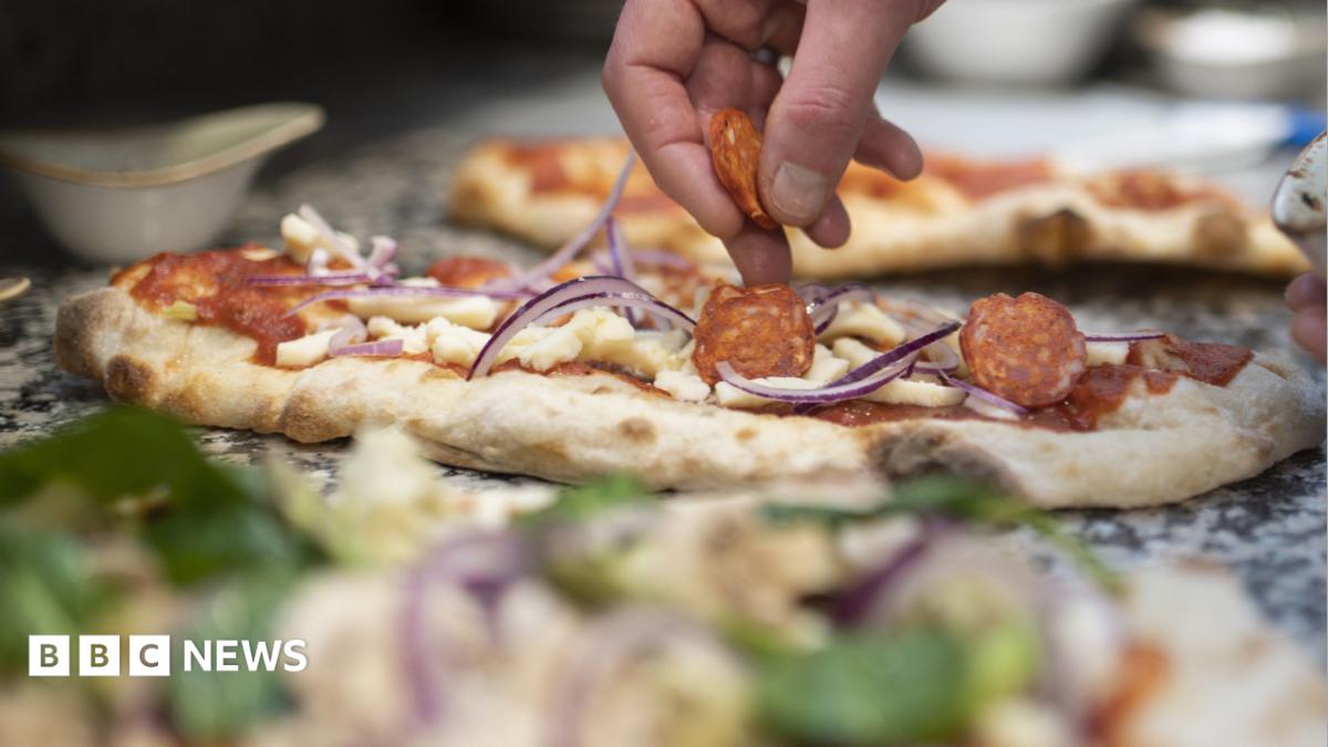 A robot arm hovers over a pizza