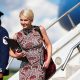 Natalie Harp walks off Air Force One wearing a sleeveless printed red dress. She is smiling and has a laptop and several phones in her hands.