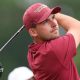 Jack Whaley, in red golf shirt and cap, tees off and watches his shot