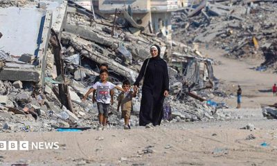 A Palestinian woman walks with children along a path lined with piles of rubble in the Sheikh Radwan neighbourhood of Gaza City