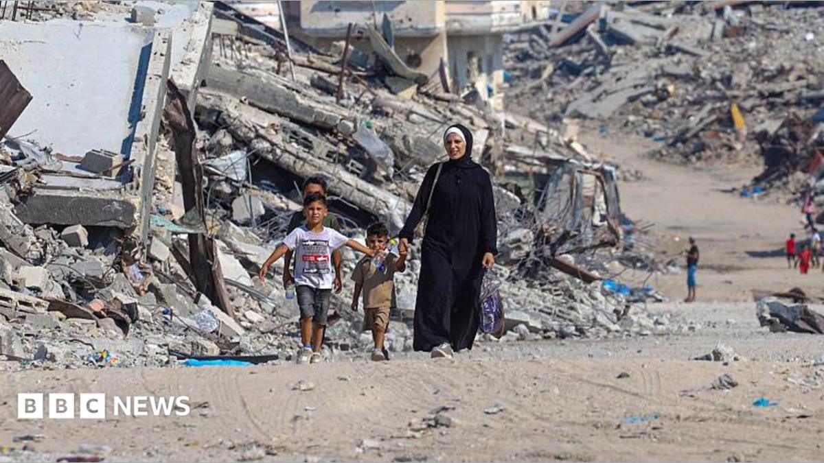 A Palestinian woman walks with children along a path lined with piles of rubble in the Sheikh Radwan neighbourhood of Gaza City