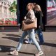 A woman in jeans and carrying a large tote bag walking along a high street. She is seen in profile against the backdrop of a shop window in London and other shoppers are in the background