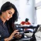 A female office worker sitting in front of a laptop and looking at her phone