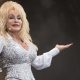 Dolly Parton wears a white shirt and bedazzled white and silver waistcoat.