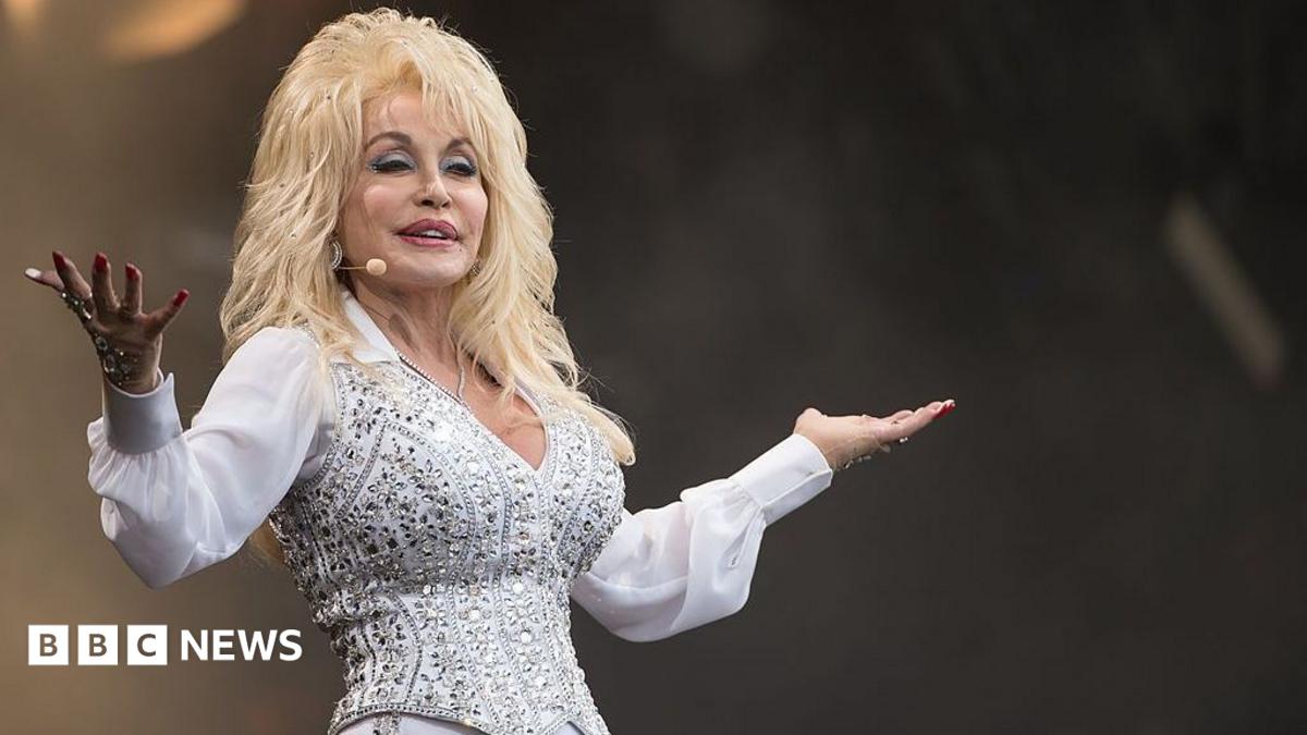 Dolly Parton wears a white shirt and bedazzled white and silver waistcoat.