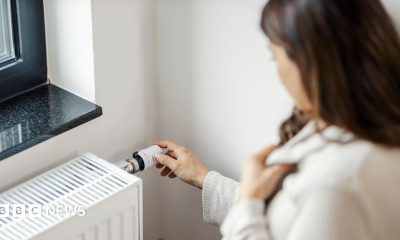 Partial side view of a woman who is holding her jumper close around her neck with one hand and turning up her radiator with the other