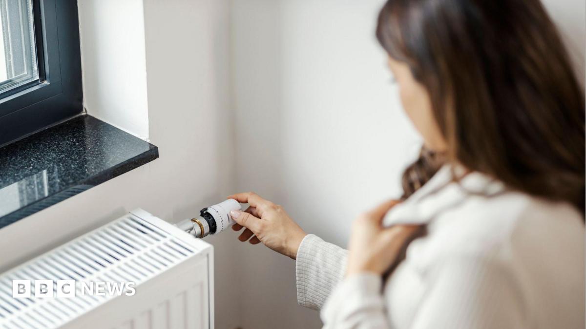 Partial side view of a woman who is holding her jumper close around her neck with one hand and turning up her radiator with the other