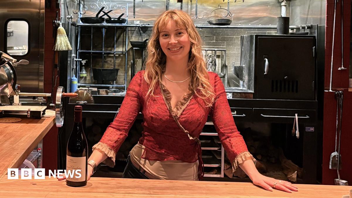 Caroline Kraetzer stands behind a bar, with her hands on the counter.