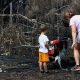 A woman and a toddler stand by charred ground and burned plants.