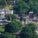 An aerial image of the White House, a large white building with tall classic columns. To the right of the building there's a large construction site, with scaffolding and cranes building a new structure.