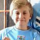 A boy in a sky blue Coventry City home shirt is smiling at the camera