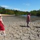 Three people standing on cracked earth of a dried out mud bed of Hollow Pond in East London on 11th August 2026