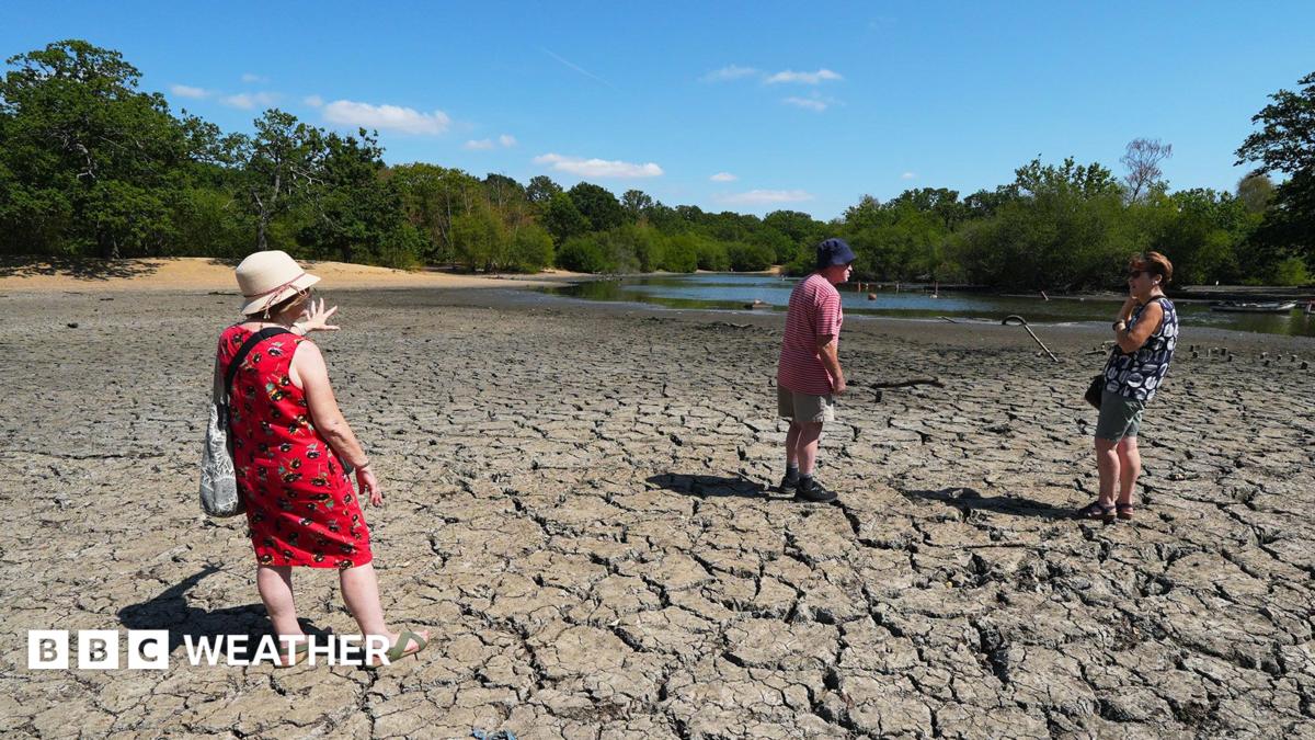 Three people standing on cracked earth of a dried out mud bed of Hollow Pond in East London on 11th August 2026
