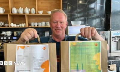 A man, Barry Ashley, stood in a cafe holding two paper bags out in front of him.