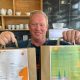 A man, Barry Ashley, stood in a cafe holding two paper bags out in front of him.