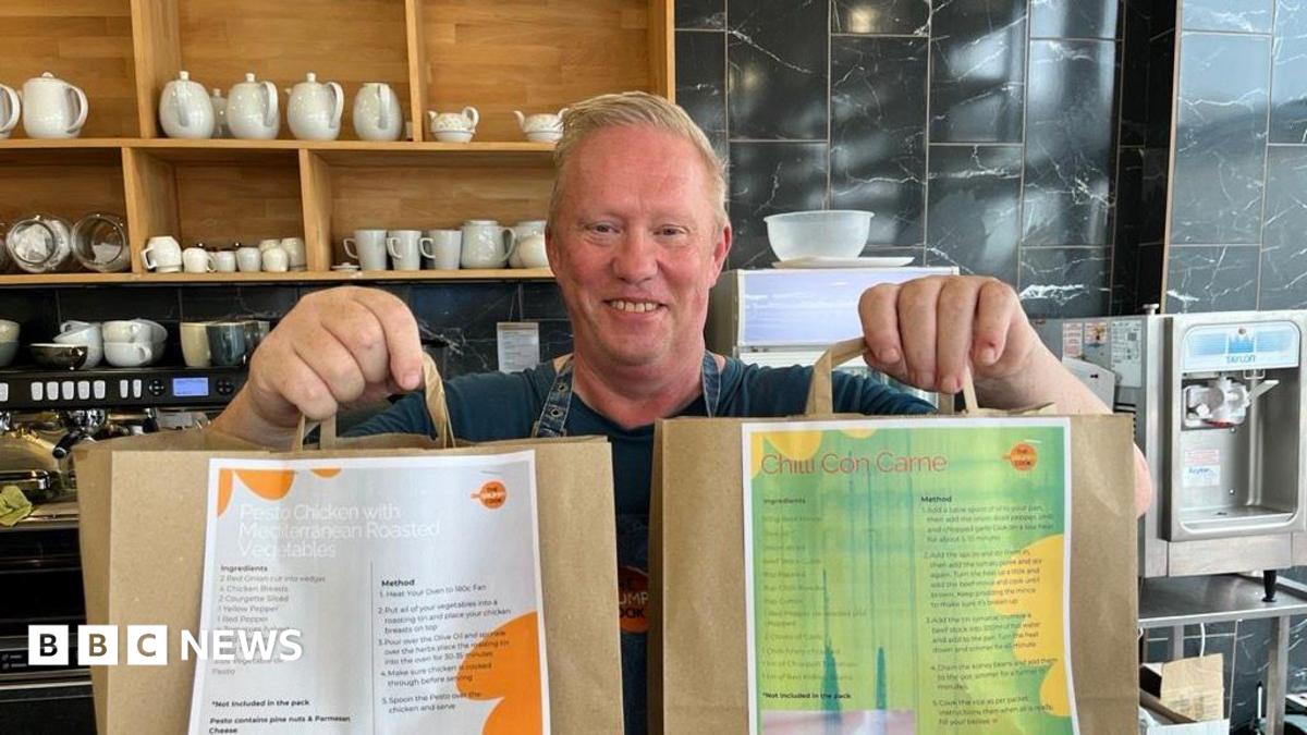A man, Barry Ashley, stood in a cafe holding two paper bags out in front of him.