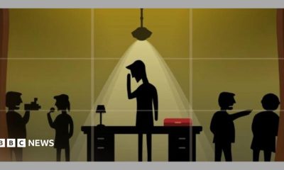 A screenshot from the game No 10: Full Confidence. It shows five silhouettes with one in the centre with their hand to their head, underneath a light and in front of a table with a red box. Two silhouettes are either side, one with a microphone, another filming them.