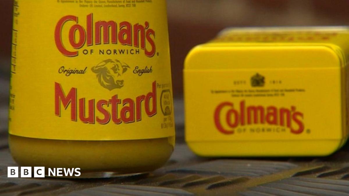 A jar and tin of Colman's Mustard propped up on a surface next to each other. The tin of mustard has been laid on its side. The packaging on each item is a mustard yellow and the label reads, Colman's of Norwich, original English Mustard.
