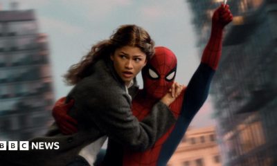 Spider-Man swings through the city on web whilst holding MJ, played by Zendaya.