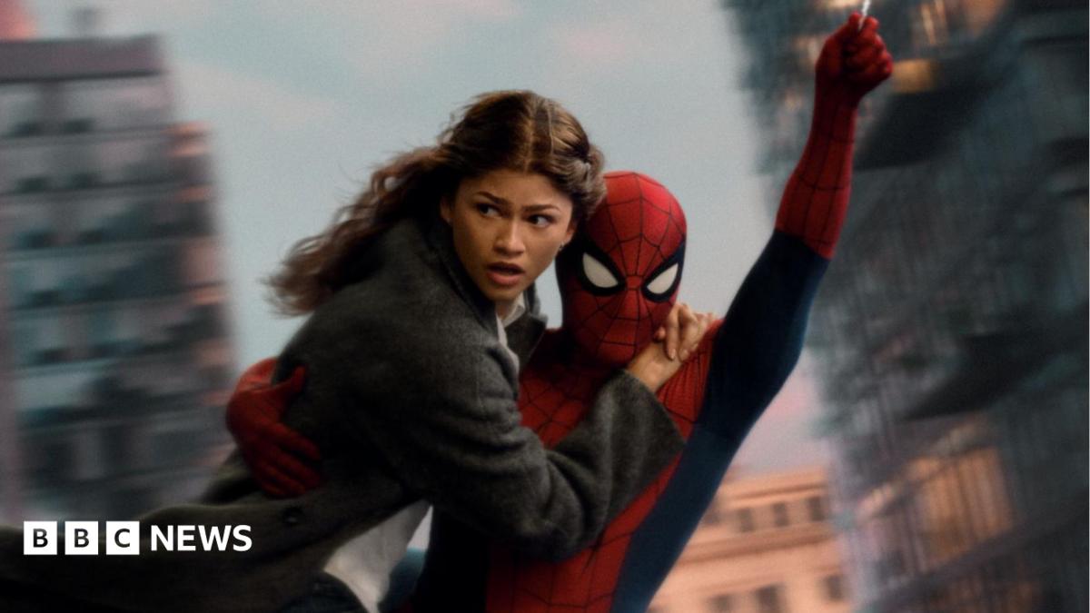 Spider-Man swings through the city on web whilst holding MJ, played by Zendaya.