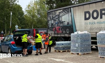People from South East Water putting bottles of water from the water station into a blue car. There are five people in the image, and they are all wearing high-vis vests.