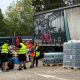 People from South East Water putting bottles of water from the water station into a blue car. There are five people in the image, and they are all wearing high-vis vests.
