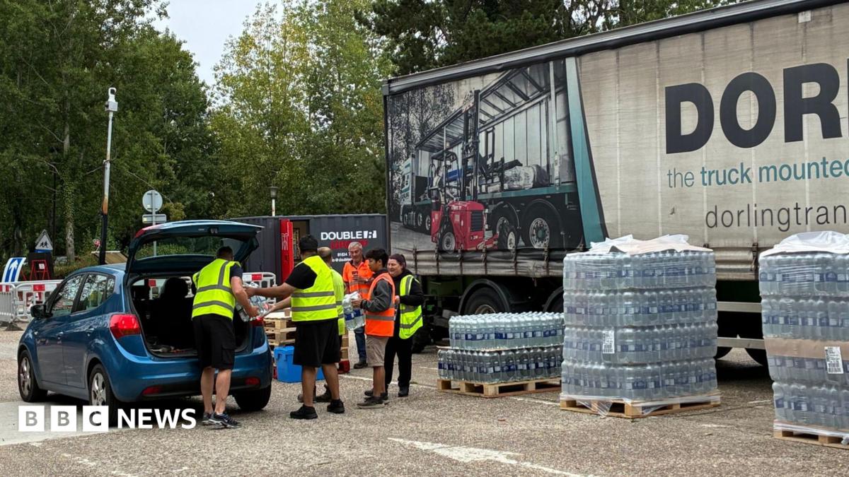 People from South East Water putting bottles of water from the water station into a blue car. There are five people in the image, and they are all wearing high-vis vests.