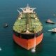 Stock image of an oil tanker pictured front on, with several tugs surrounding the ship