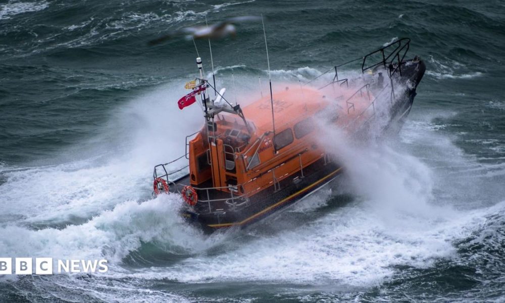 A Shannon class lifeboat in rough swell with a wave breaking over it.