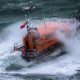 A Shannon class lifeboat in rough swell with a wave breaking over it.