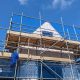 Stock photo shows the shell of a house with scaffolding around it against a blue cloudy sky, illustrating the building of new housing.