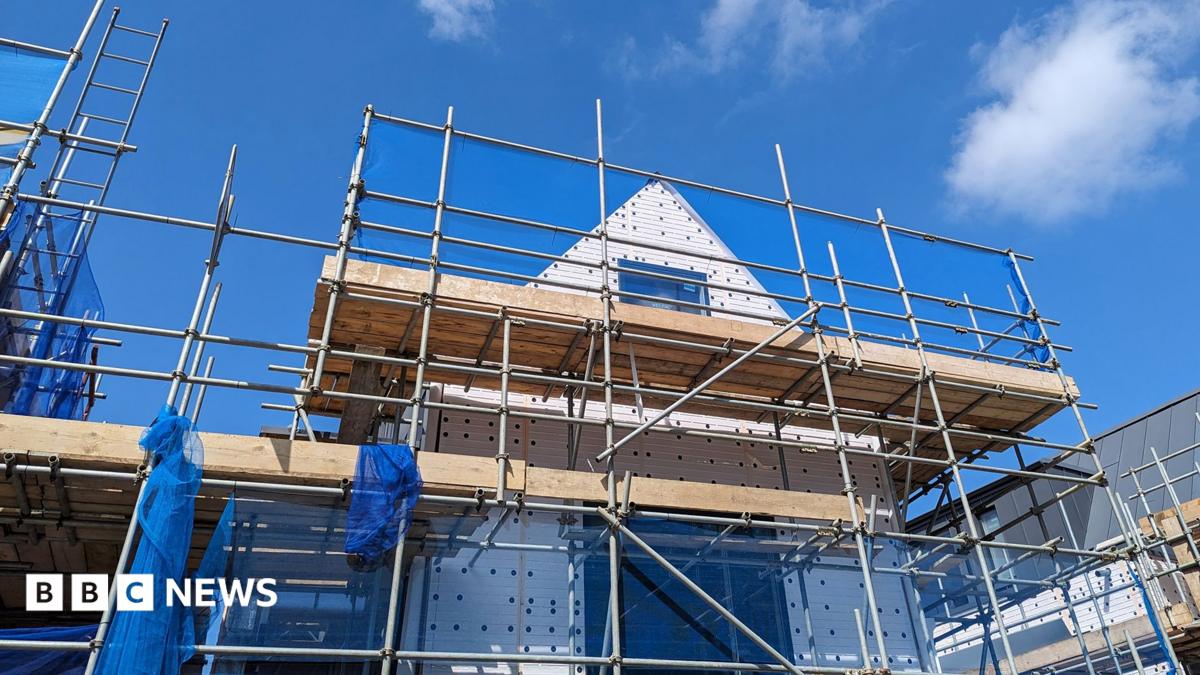 Stock photo shows the shell of a house with scaffolding around it against a blue cloudy sky, illustrating the building of new housing.