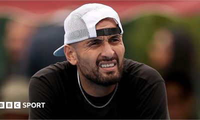 Nick Kyrgios, wearing a baseball cap backwards, looks out while slightly squinting