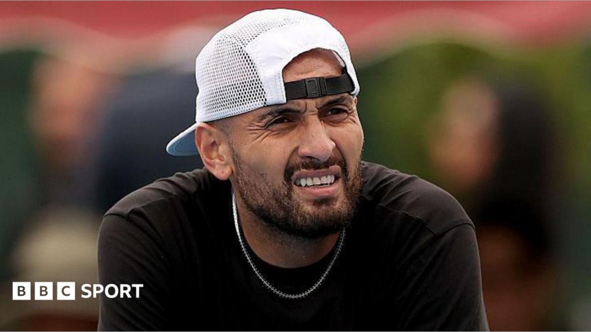 Nick Kyrgios, wearing a baseball cap backwards, looks out while slightly squinting