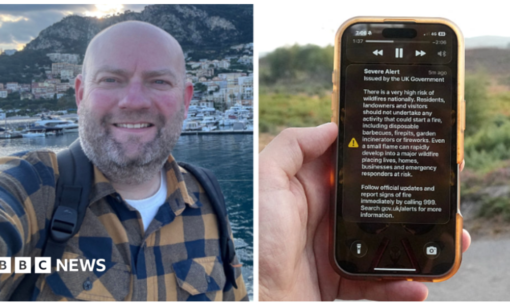 A man holds a phone in front of a green field. The phone is displaying the UK government wildfire alert.