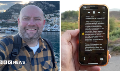 A man holds a phone in front of a green field. The phone is displaying the UK government wildfire alert.