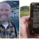 A man holds a phone in front of a green field. The phone is displaying the UK government wildfire alert.
