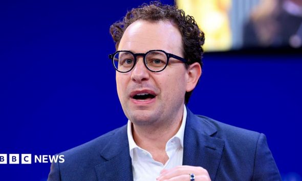 Anthropic CEO Dario Amodei speaking on a stage while gesturing with his hands.