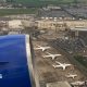 View from a plane shows blue engine of plane and four aircraft on tarmac outside low-rise terminal buildings.