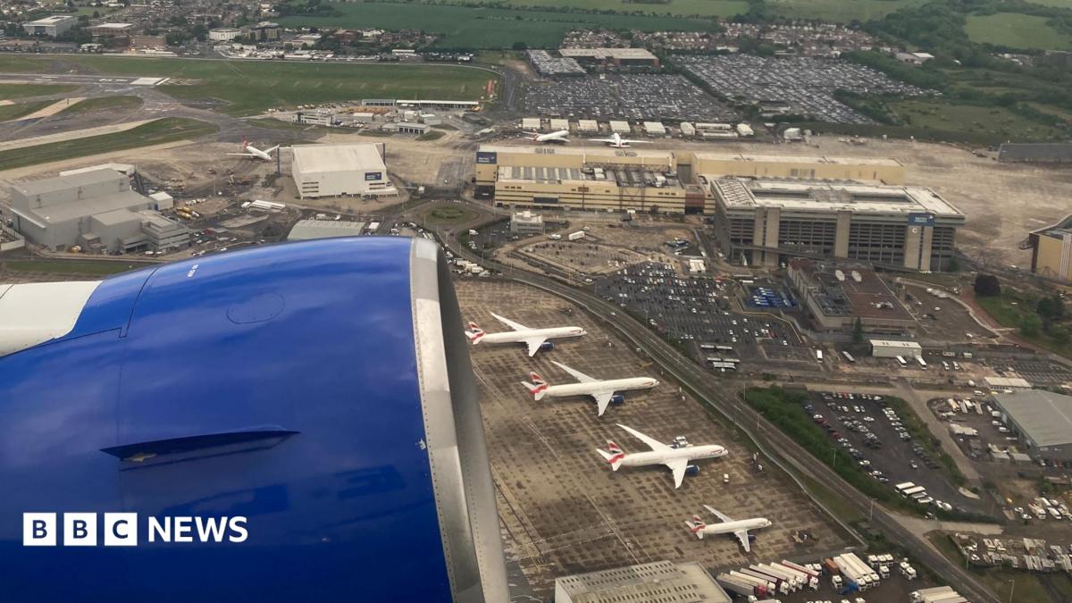 View from a plane shows blue engine of plane and four aircraft on tarmac outside low-rise terminal buildings.