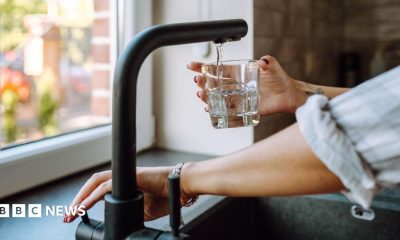 Hands only image of someone turning on a mixer tap to fill a glass of water