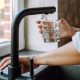 Hands only image of someone turning on a mixer tap to fill a glass of water