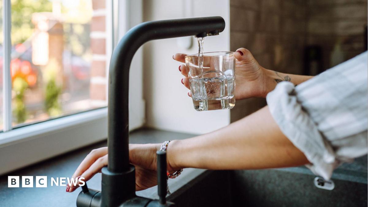 Hands only image of someone turning on a mixer tap to fill a glass of water