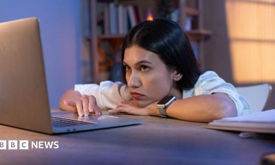 A forlorn young woman slumped over a desk looking at a laptop